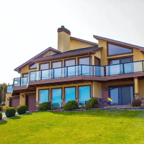 Large multi-level hillside home finished in warm gold and brown stucco with glass railings